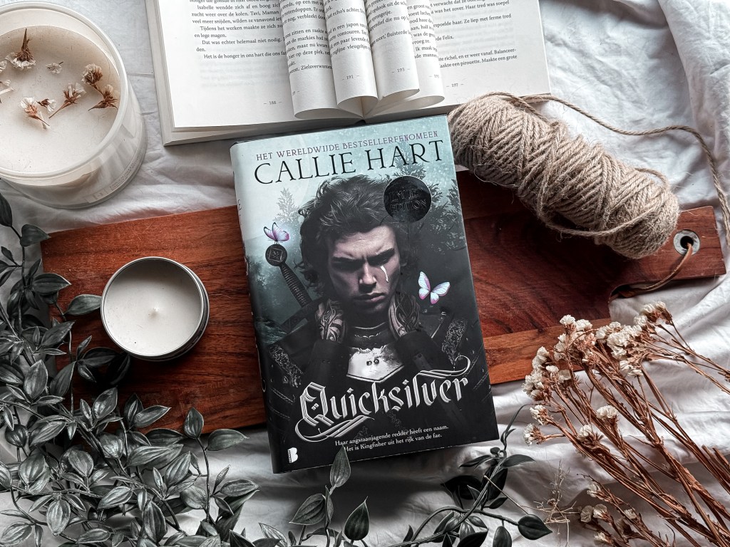 Een sfeervolle flatlay van het boek Quicksilver van Callie Hart met een donkere, mysterieuze cover. Het boek ligt op een houten plank, omringd door kaarsen, touw en droogbloemen, met een open boek op de achtergrond. De setting straalt een warme en rustieke fantasy-vibe uit.