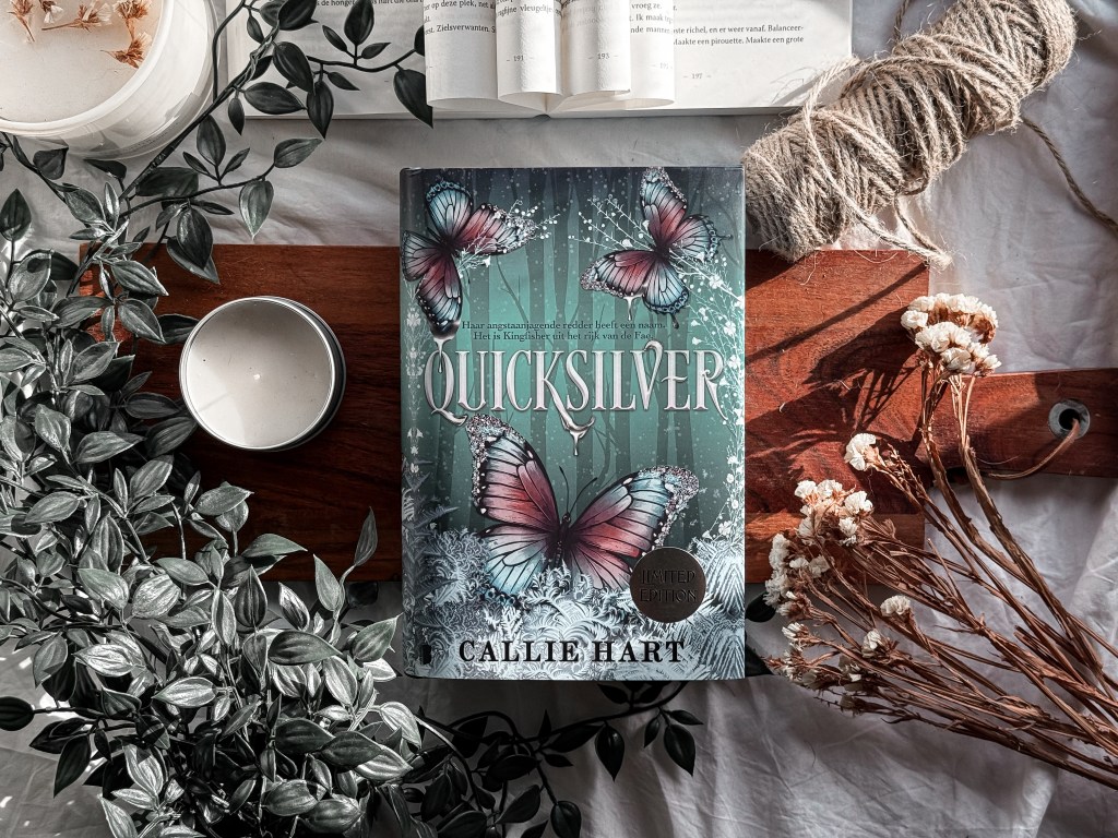 Een prachtige flatlay van de Limited Edition van Quicksilver van Callie Hart, met een betoverende cover vol glinsterende vlinders. Het boek ligt op een houten plank, omringd door kaarsen, droogbloemen en touw, wat zorgt voor een sprookjesachtige en elegante sfeer.