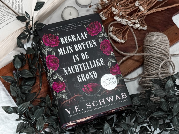 A flatlay of the book Bury Our Bones in the Midnight Soil (limited edition) by V.E. Schwab, surrounded by ivy, dried flowers, twine and open books. The cover is black with striking pink roses and a silver sticker that reads “Limited Edition".